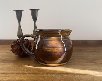 May include: A brown ceramic pitcher with a white rim and a handle. The pitcher has a glossy finish and is sitting on a wooden surface.