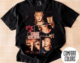 May include: A black short-sleeve t-shirt featuring a collage of four photographic portraits of a person with blonde hair, accented by red and orange lily flowers and a digital music player interface graphic displaying the text who Jimin.
