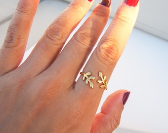 May include: A gold ring with a delicate leaf design. The ring is worn on the middle finger of a hand with red nail polish.