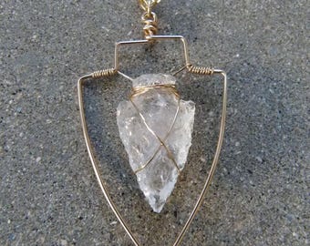 May include: A gold chain necklace with a clear quartz crystal pendant in a gold wire frame shaped like an arrowhead.