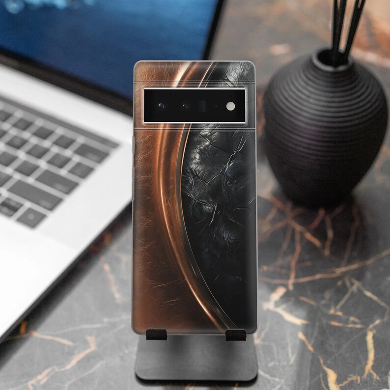 Puede incluir: Una funda de tel&eacute;fono inteligente con un dise&ntilde;o abstracto marr&oacute;n y negro. La funda tiene un borde curvo de aspecto met&aacute;lico y un centro negro texturizado. La funda del tel&eacute;fono se muestra en un soporte negro.