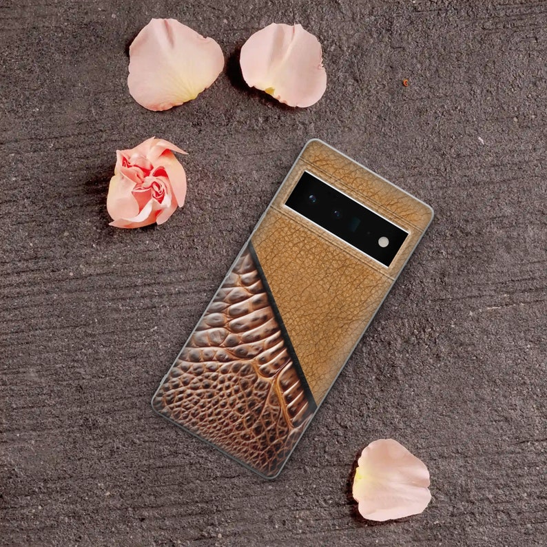 Puede incluir: Funda de tel&eacute;fono marr&oacute;n y beige con un dise&ntilde;o texturizado. La funda presenta una textura similar al cuero en la parte superior y un patr&oacute;n de piel de reptil en la parte inferior. P&eacute;talos de flores rosas decoran la imagen.