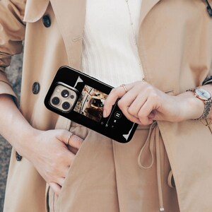 May include: Black phone case with a music player interface. The case features a black background with white sound wave graphics and a photo. The phone case is held by a person wearing a tan trench coat and a gold watch.