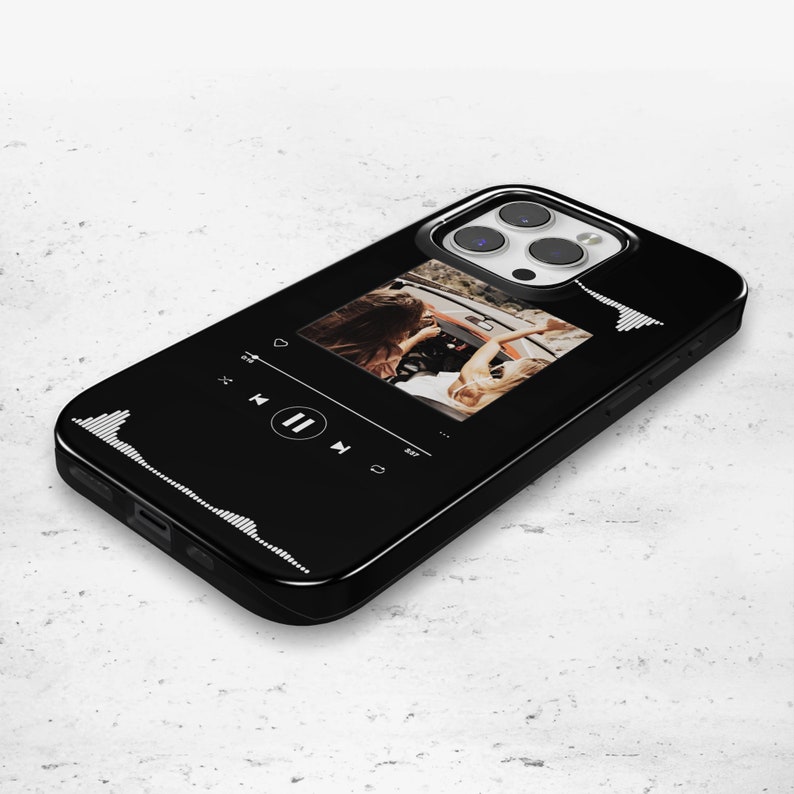 May include: Black smartphone case featuring a music player interface design. The case displays a photo of two people in a car. White sound wave graphics are on the left and right sides of the case. The phone case has a glossy finish.