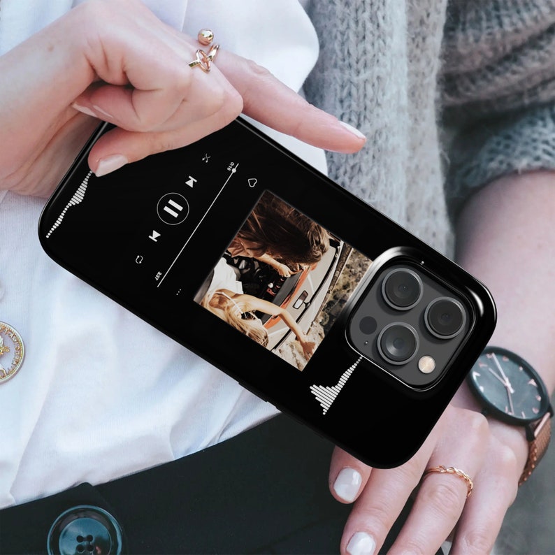 May include: Black smartphone case featuring a music player interface with a photo of two people in a car. The case has a glossy finish and a camera cutout. The design includes a waveform graphic on the sides.