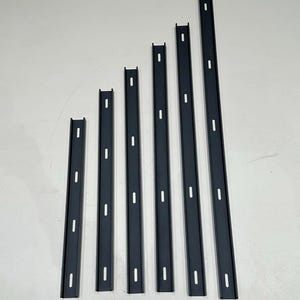 May include: Six dark grey metal shelf support brackets of varying lengths, arranged vertically. Each bracket has a series of evenly spaced, rectangular holes. The brackets are designed for mounting shelves and provide structural support.