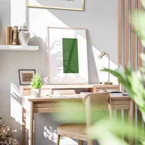 Puede incluir: Una impresi&oacute;n enmarcada con un fondo verde y caligraf&iacute;a &aacute;rabe blanca. La impresi&oacute;n est&aacute; colgada en una pared sobre un escritorio de madera con una silla y una l&aacute;mpara.