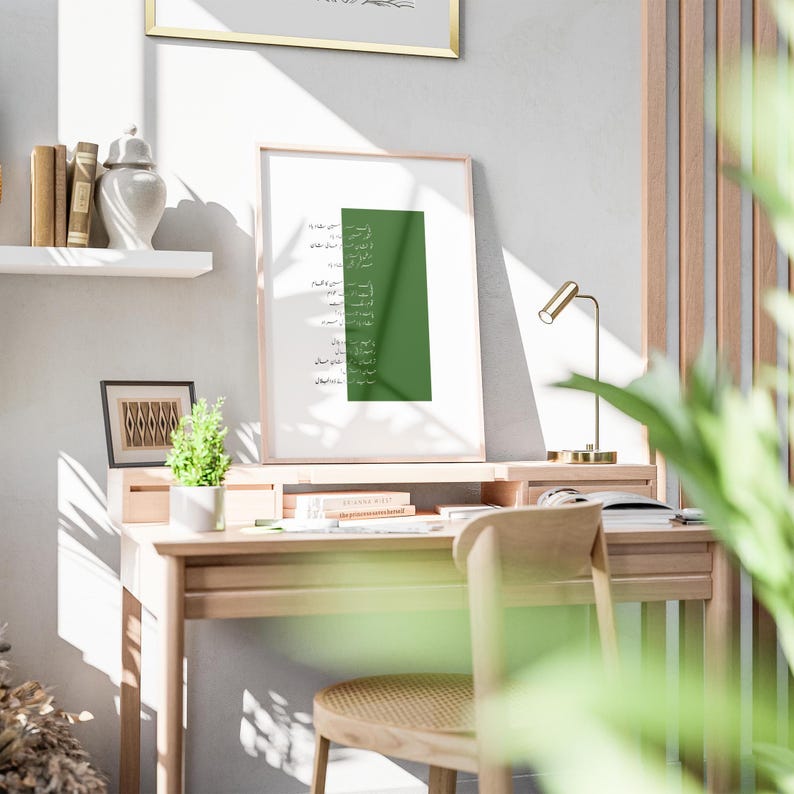 Puede incluir: Una impresi&oacute;n enmarcada con un fondo verde y caligraf&iacute;a &aacute;rabe blanca. La impresi&oacute;n est&aacute; colgada en una pared sobre un escritorio de madera con una silla y una l&aacute;mpara.