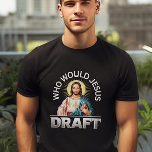 Könnte beinhalten: Schwarzes T-Shirt mit einem weißen Kreis-Motiv, das eine Darstellung von Jesus zeigt, der einen Football hält. Der Text "Who Would Jesus Draft" ist in Weiß und Silber gedruckt.