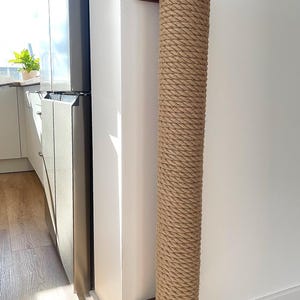 May include: A cat scratching post made of natural rope and wood. The post is cylindrical and mounted on a wall. The rope is tightly wound around the post, and the wooden ends are a dark brown color. This cat furniture is designed to provide a place for cats to scratch.