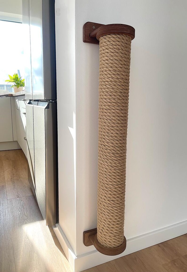 May include: A cat scratching post made of natural rope and wood. The post is cylindrical and mounted on a wall. The rope is tightly wound around the post, and the wooden ends are a dark brown color. This cat furniture is designed to provide a place for cats to scratch.