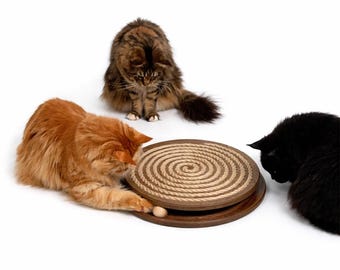 May include: A cat toy with a spiral rope design and a wooden base. Three cats of different colors, including orange, brown, and black, are interacting with the toy. The cats are focused on the toy, suggesting playful engagement.