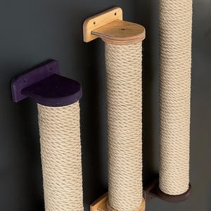May include: Three cat scratching posts with a natural rope texture and wooden platforms. The platforms are in purple, light brown, and dark brown. The posts are mounted on a dark gray wall.