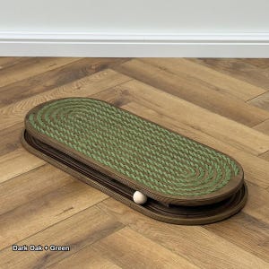 May include: Dark oak and green cat toy with a wooden frame and a green rope surface. A small white ball is in the track. The text "Dark Oak + Green" is at the bottom left.