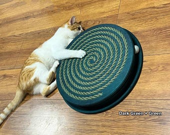 May include: A dark green cat toy with a spiral rope design and a white ball, with a white and orange cat lying next to it. The text "Dark Green + Green" is visible on the toy.