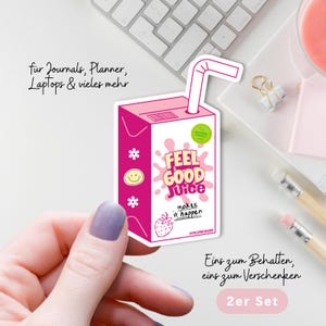 Könnte beinhalten: Ein rosa-weißer Aufkleber in Form eines Saftkartons mit Strohhalm. Der Aufkleber trägt die Aufschrift "FEEL GOOD Juice" mit einer Erdbeer-Illustration. Zusätzlicher Text lautet "makes it happen" und "2er Set".