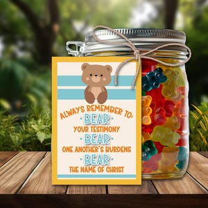 Puede incluir: Un tarro de cristal lleno de ositos de goma de colores, atado con hilo, y una etiqueta amarilla. La etiqueta presenta un oso de dibujos animados y el texto "Always Remember To Bear Your Testimony, Bear One Another's Burdens, Bear The Name of Christ."