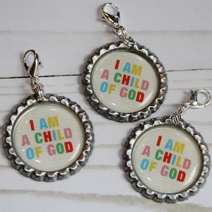 May include: Three silver bottle cap charms with a white background and colorful text that reads "I AM A CHILD OF GOD". Each charm has a silver lobster clasp.