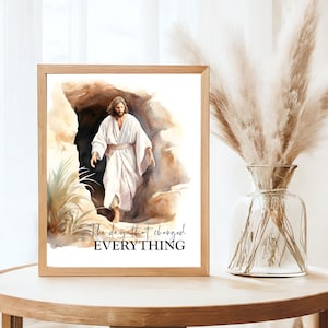 May include: A watercolour painting of Jesus Christ emerging from a cave. The painting is framed in a light wood frame and has the text "The day that changed EVERYTHING" at the bottom.