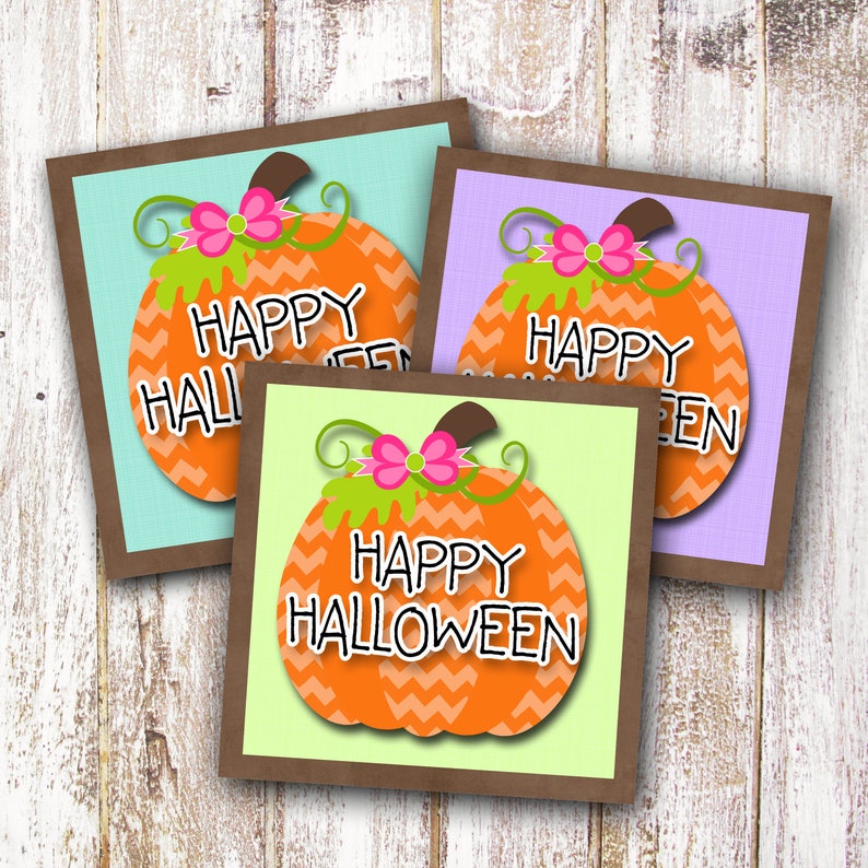 May include: Three printable gift tags featuring orange pumpkins with a chevron pattern and pink bows. The text on the tags reads "Happy Halloween", "Happy Hallowee", and "Happy Green".