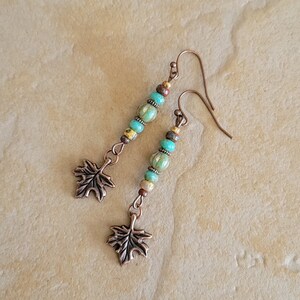 May include: A pair of dangle earrings with turquoise and gold beads and a copper leaf charm.