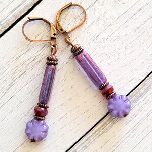 May include: Purple and red glass bead earrings with a flower-shaped bead and a copper-toned hook.