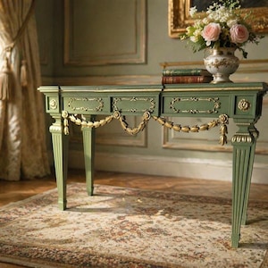May include: An antique green console table with gold detailing. The table has decorative carvings and a gold garland. A vase of pink roses and books are on top. The table is on a patterned rug.