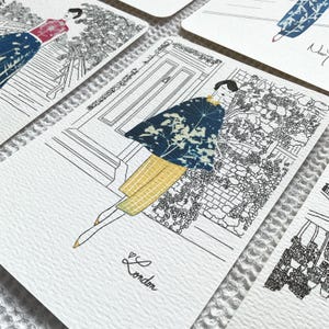 May include: A black and white illustration of a woman wearing a blue and white patterned cape and yellow pants. The woman is standing in front of a building with a door and a garden. The text "London" is written below the woman.