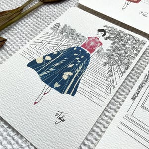 May include: A black and white illustration of a woman wearing a red and white patterned top and a blue and white patterned skirt. She is walking on a bridge with a Japanese garden in the background. The image is signed "Tokyo" in the bottom right corner.