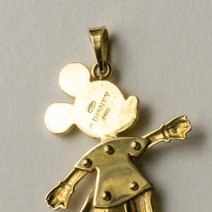 Puede incluir: Un colgante dorado con la forma de Mickey Mouse. El colgante presenta a Mickey en una pose cl&aacute;sica, con los brazos extendidos. La parte posterior del colgante est&aacute; estampada con "&copy; DISNEY" e "ITALY".