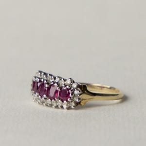 Peut inclure: Une bague en or avec une rangée de cinq rubis rouge foncé taille ovale sertis sur une base en métal argenté. Le groupe central de rubis est rehaussé de petites pierres claires taille ronde sur les bords, formant un motif multi-pierres.