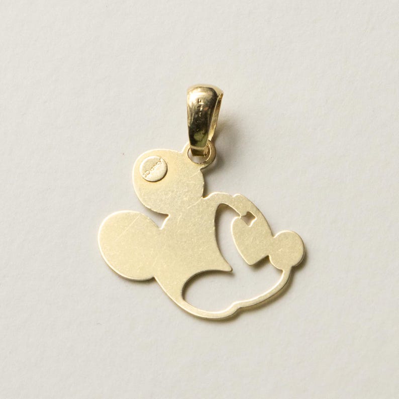 K&ouml;nnte beinhalten: Goldfarbener Anh&auml;nger in Form einer Zeichentrickfigur. Der Anh&auml;nger hat oben eine Schlaufe f&uuml;r eine Kette und ein stilisiertes Design mit abgerundeten Formen und einem kleinen Kreis.