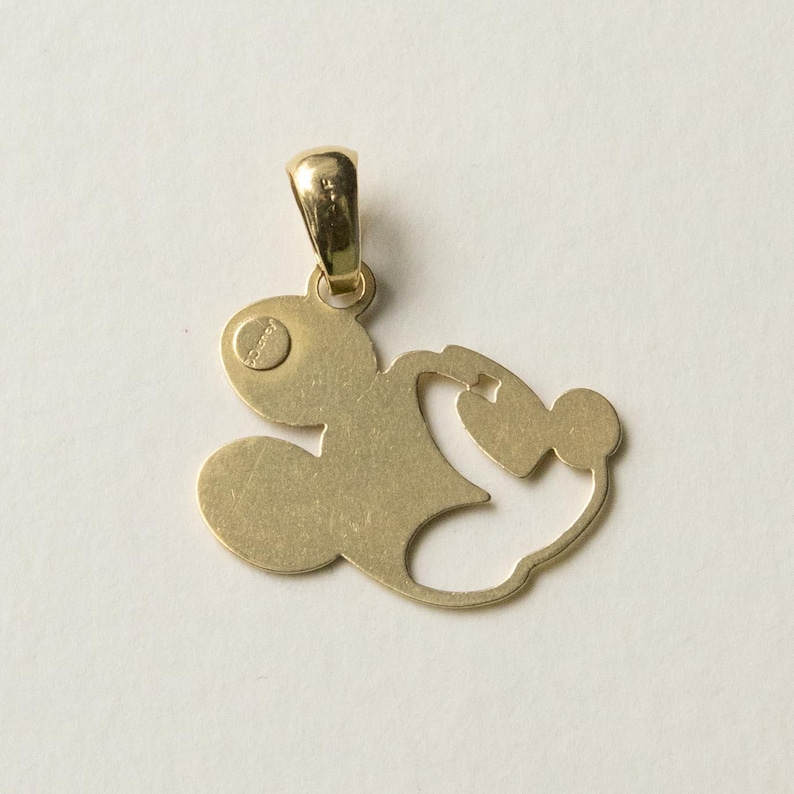 K&ouml;nnte beinhalten: Goldfarbener Anh&auml;nger in Form einer Zeichentrickfigur. Der Anh&auml;nger hat oben eine Schlaufe f&uuml;r eine Kette und ein kleines, kreisf&ouml;rmiges Detail mit Text. Das Design ist eine Silhouette einer ber&uuml;hmten Zeichentrickfigur.