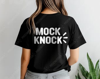 May include: Black t-shirt with the white text "MOCK KNOCK" and a stylized lightning bolt graphic. The shirt is a classic crew neck style and is being worn by a person. The background is a neutral color.