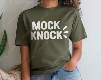 May include: Olive green t-shirt with the white text "MOCK KNOCK" in a bold, sans-serif font. The shirt has short sleeves and a relaxed fit. The model is wearing blue jeans.