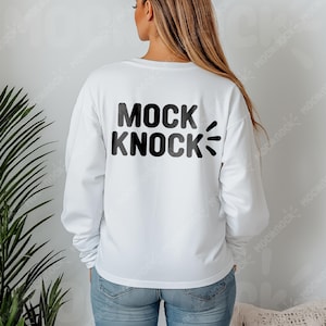 May include: White long-sleeve sweatshirt with the text "MOCK KNOCK" in black and gray block letters on the back. The design includes stylized sound effect lines. The model is wearing blue jeans.
