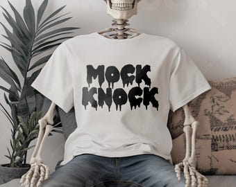 May include: A white t-shirt with black dripping text that reads "MOCK KNOCK". The shirt is being worn by a skeleton.