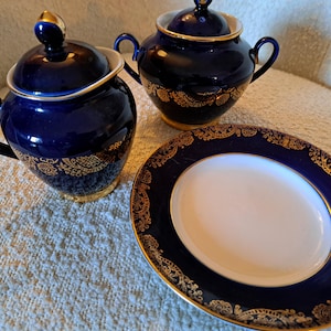 Può includere: Un servizio da tè in tre pezzi di colore blu scuro con dettagli in filigrana dorata. Il set include una zuccheriera con coperchio, una lattiera e un piatto ovale. I bordi e le maniglie sono dorati.