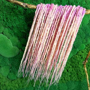 Peut inclure: Un ensemble de dreadlocks synthétiques roses et blanches suspendues sur un fond de mousse verte.