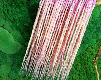 May include: A set of pink and white synthetic dreadlocks hanging against a green moss background.