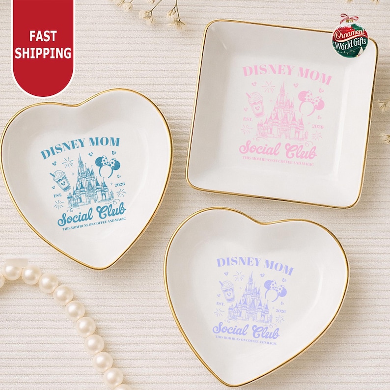 three decorative dishes with Disney-themed designs, including a heart-shaped dish, a square dish, and a smaller heart-shaped dish. The dishes are placed on a white surface, and there is a string of pearls nearby.
