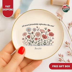 May include: A round, cream-colored decorative plate with a gold rim. The plate features a floral design in shades of pink, red, and blue, with the text "A sweet friendship refreshes the soul" and "Prov:27:9".