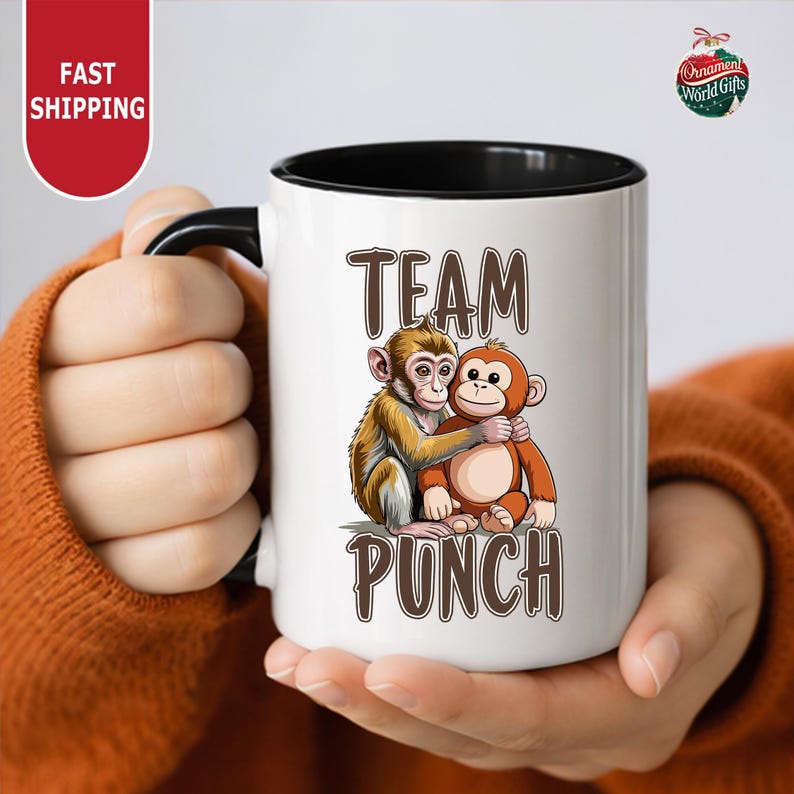 A person is holding a white mug with a cartoon image of two monkeys hugging each other.