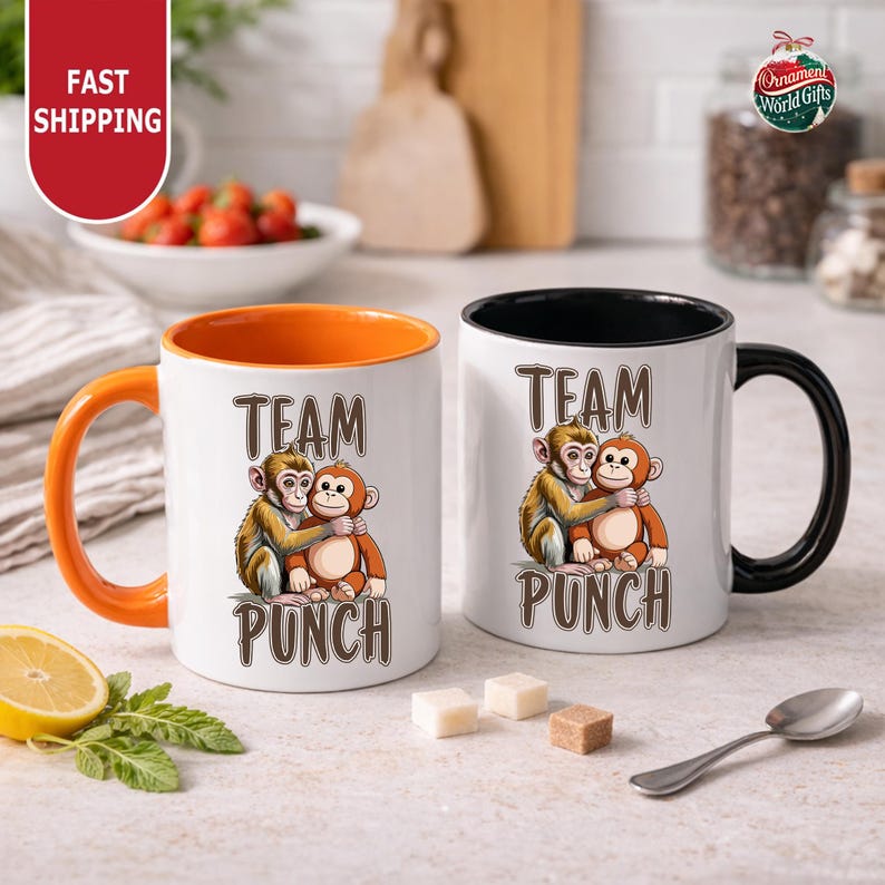 two mugs with a cartoon monkey design, one orange and one black, both with the text "TEAM PUNCH" printed on them. The mugs are placed on a kitchen counter, with various food items and utensils visible in the background.