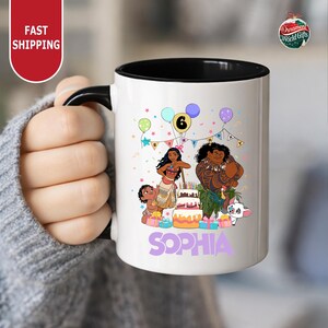 A person is holding a white mug with a colorful illustration of a group of people, including a character named Sophia, surrounded by balloons and a birthday cake.