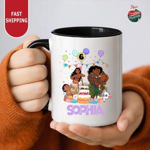 A person is holding a white mug with a colorful illustration of characters from the movie "Moana" and the text "Sophia" on it.
