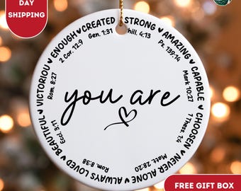 May include: White ceramic ornament with the words "you are" in black cursive script and a small heart. The ornament is surrounded by a circle of words and bible verses in black text, including "victorious", "enough", "created", "strong", "amazing", "capable", "chosen", "never alone", "always loved", and "beautiful".