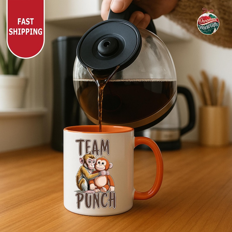 A person is pouring coffee from a coffee pot into a white mug with an orange handle, which has a cartoon monkey design and the text "TEAM PUNCH" printed on it.