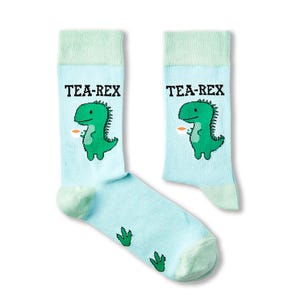 May include: A pair of light blue socks featuring a green dinosaur holding a cup of tea. The socks have the text "TEA-REX" printed on them.