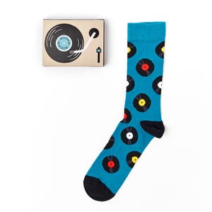 May include: A pair of blue socks with a pattern of black vinyl records. The socks have a black heel and toe. The socks are packaged in a small box with a picture of a record player.